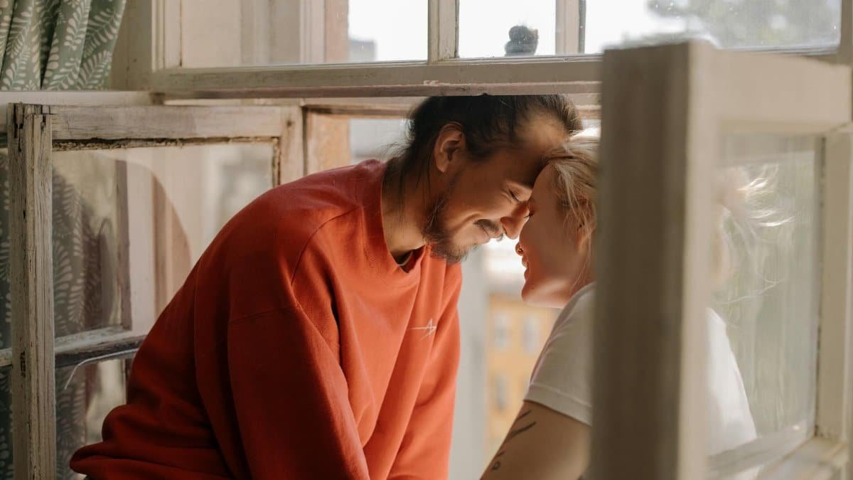 Young couple sharing a joyful moment by the window, enjoying each other's company and laughter indoors.