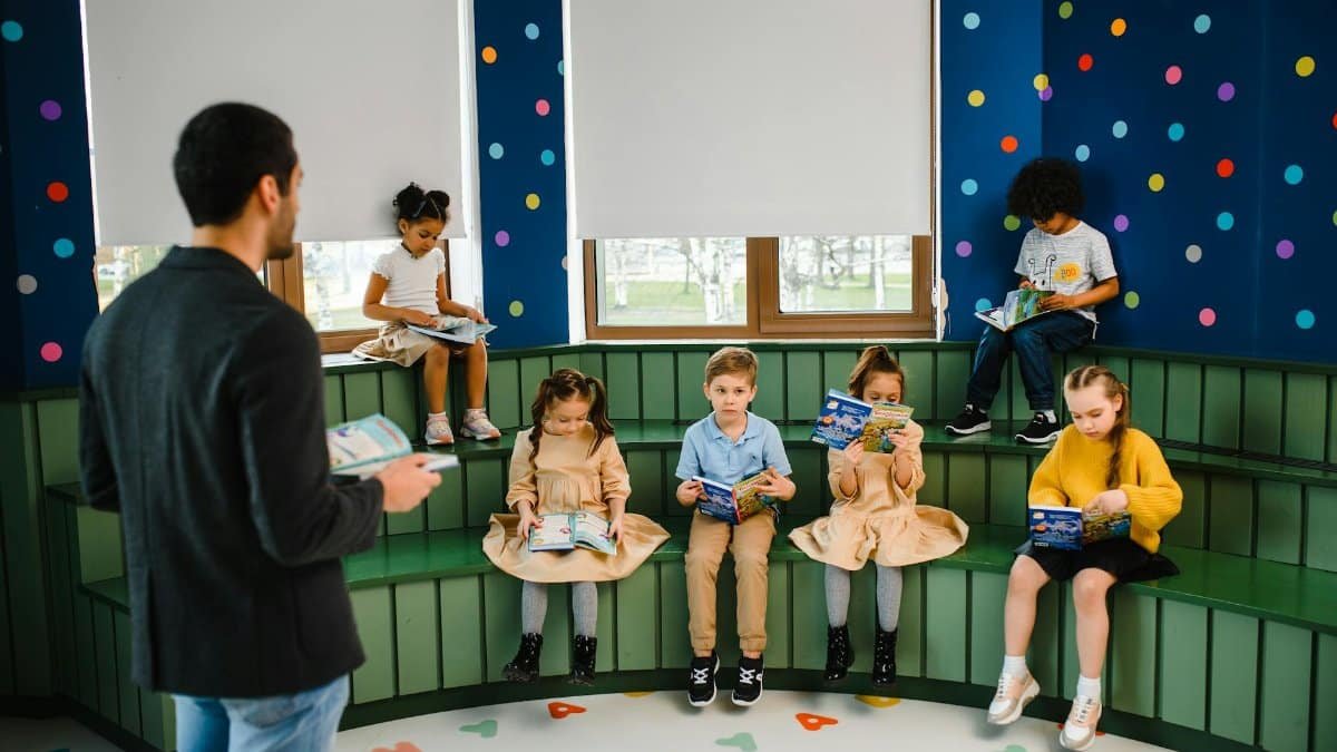Preschool teacher leading storytime with children reading books in a colorful classroom setting.