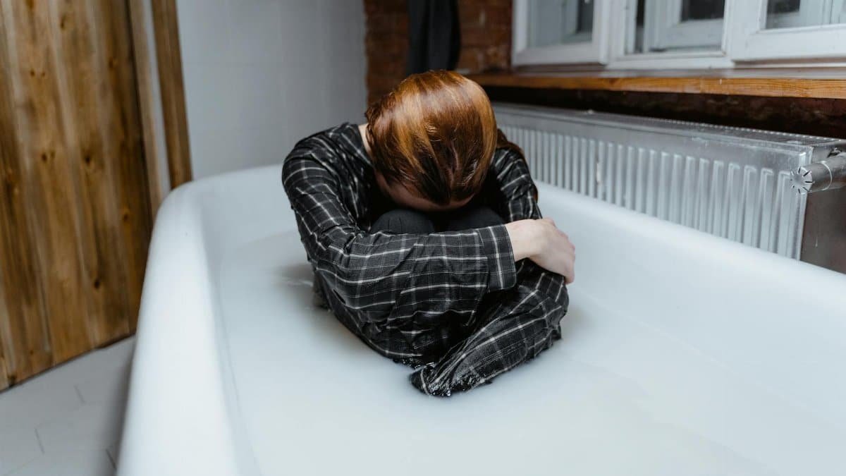 A person in a bathtub showing feelings of sadness and isolation, indoors.