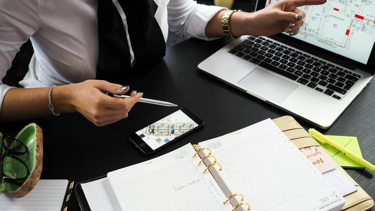 A business professional working on real estate project plans using multiple devices in an office setting.