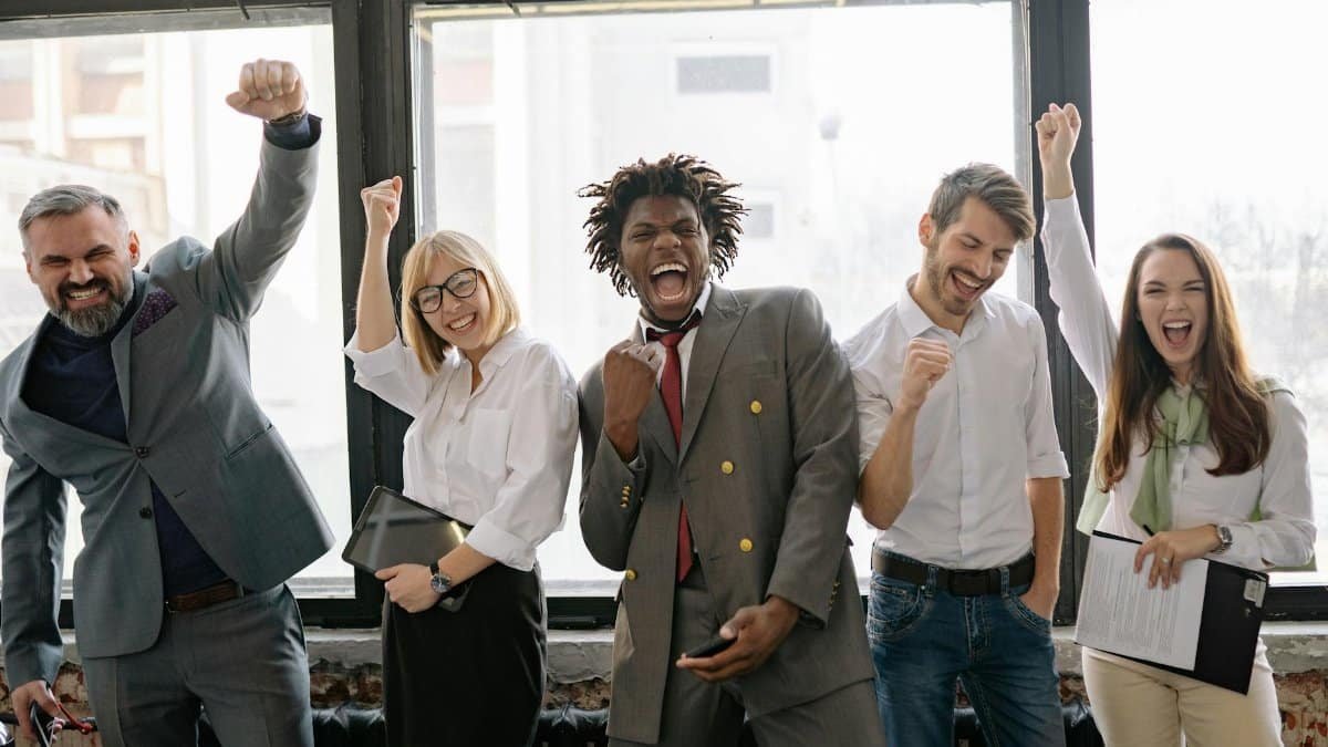 A joyful, diverse group of colleagues celebrating success indoors with cheerful expressions.