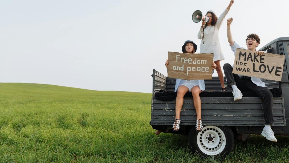 Group of young adults holding peace and freedom signs on a truck in an open field, expressing activism.