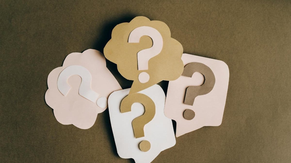 Four paper cutouts of question marks in beige and white on a brown surface, symbolizing inquiry and curiosity.