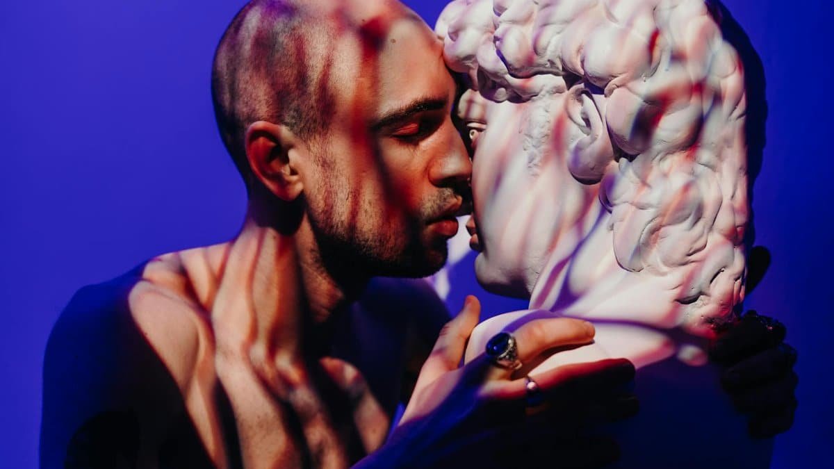 A man intimately engages with a sculpture, exploring themes of self-love and connection.