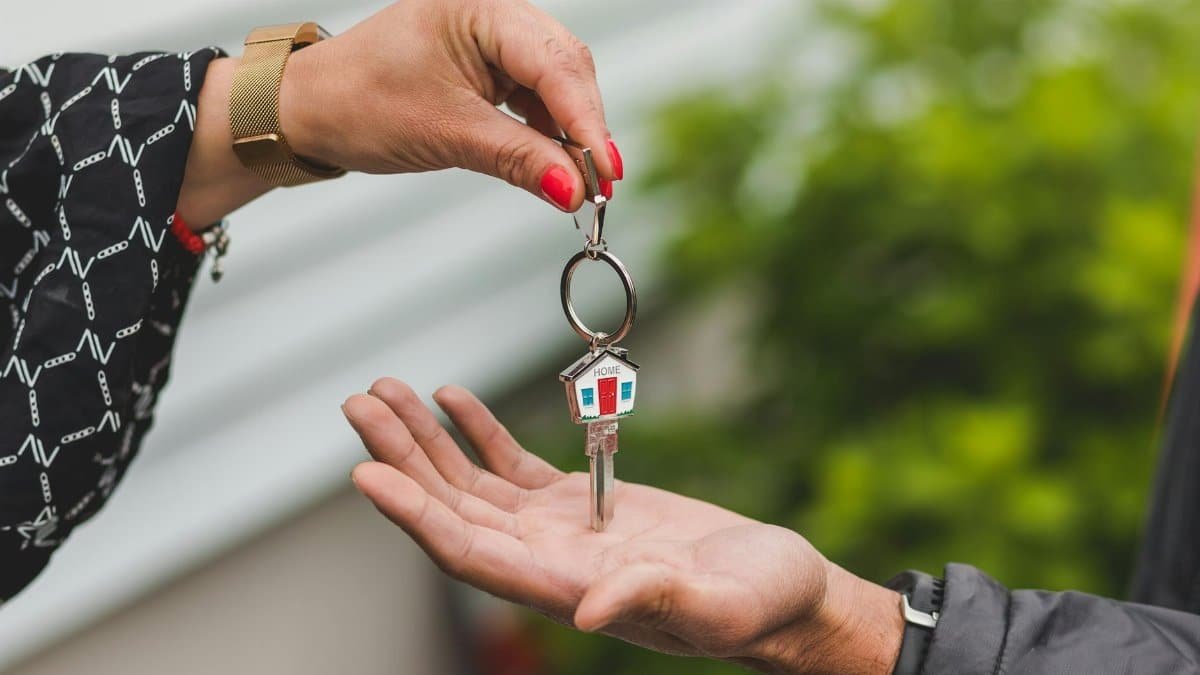 Close-up of a hand handing over a key with a house keychain, symbolizing real estate transaction.