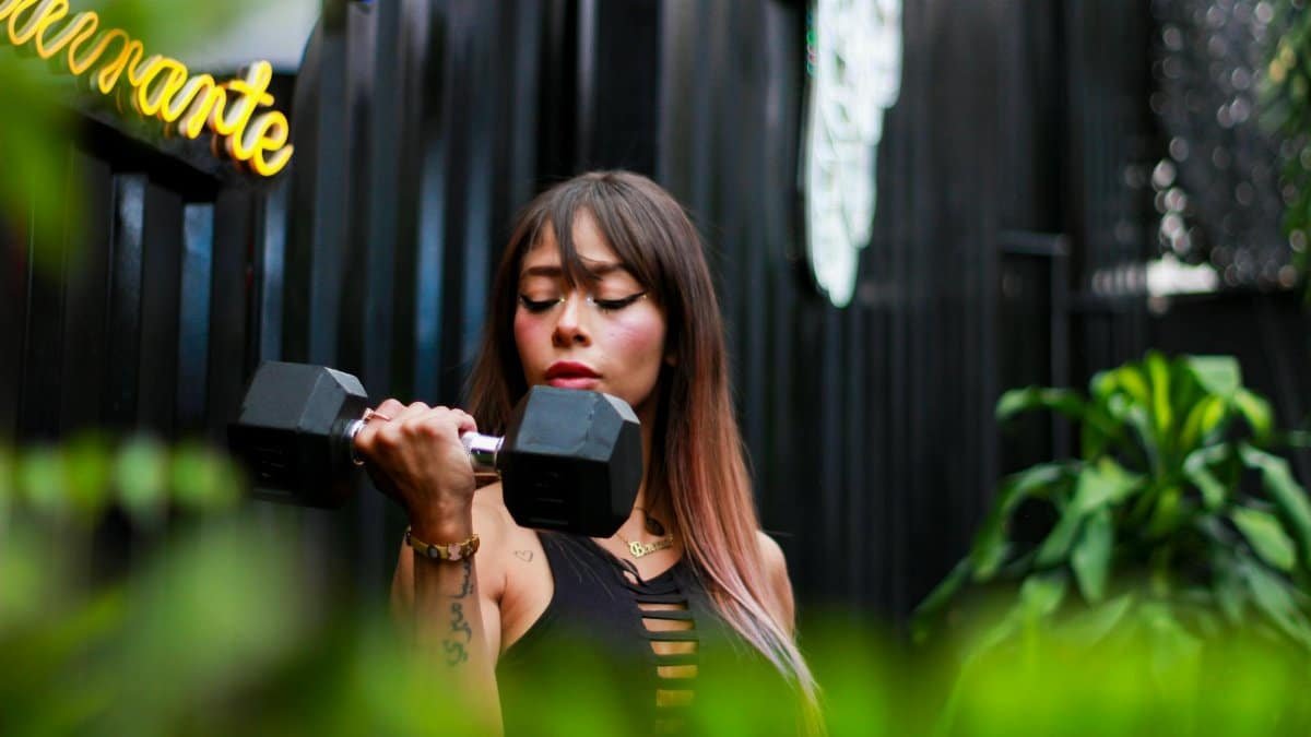 Fitness woman with long hair lifting a dumbbell outdoors, focusing on her strength training.