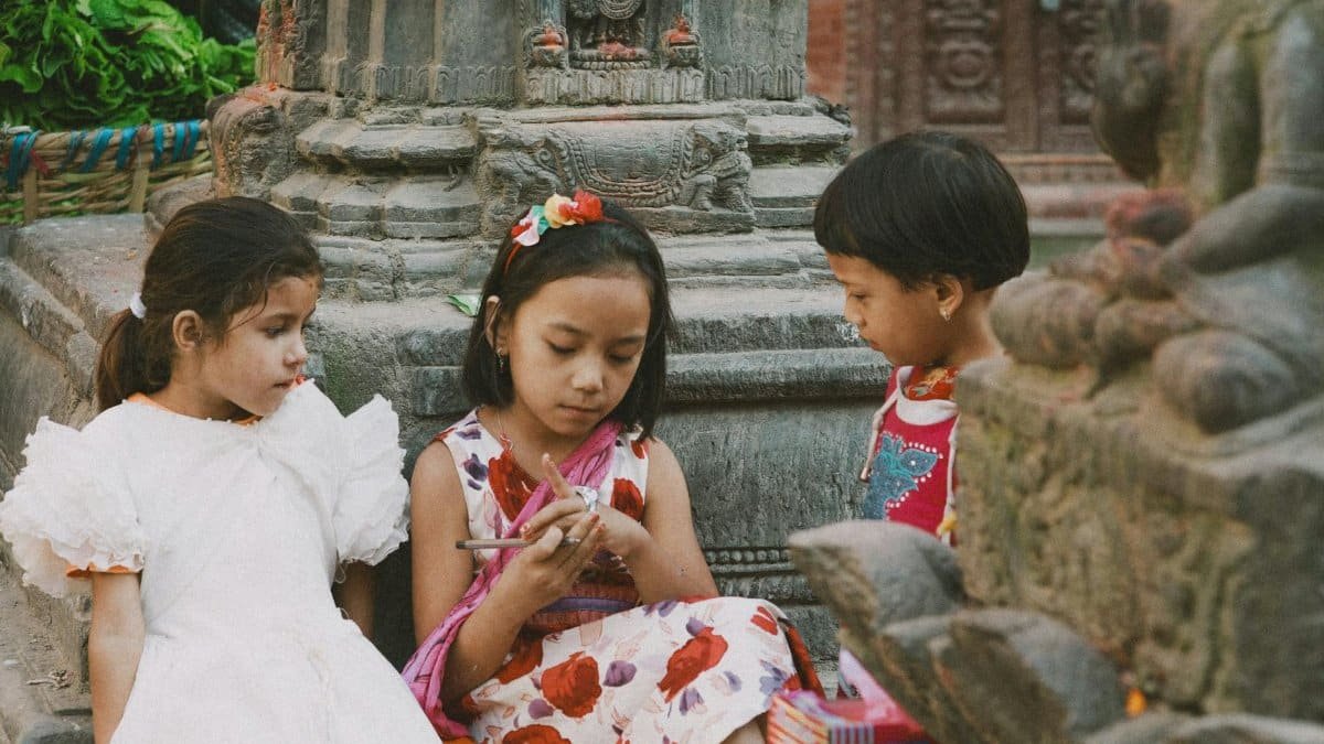 Three children sitting and playing together at an ancient stone temple outdoors.