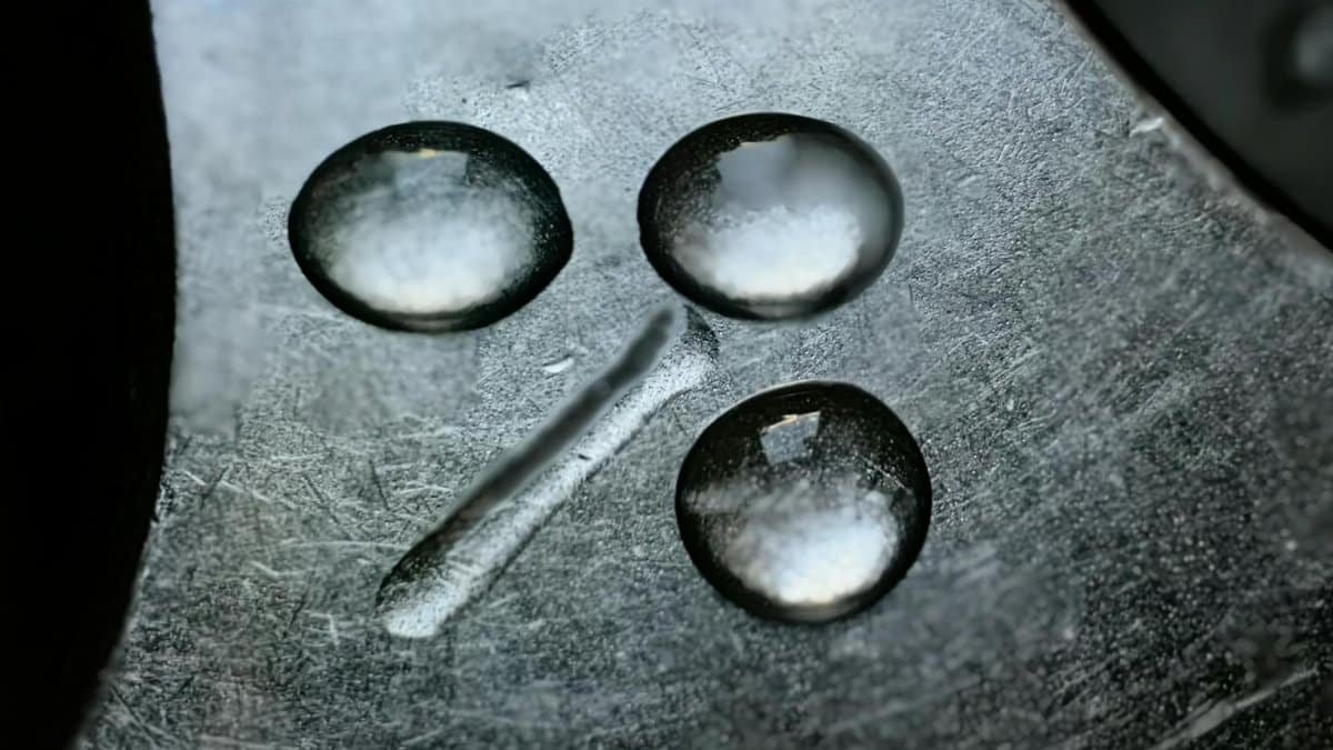 Detailed macro shot of water droplets on textured metal surface. High contrast and reflective detail.