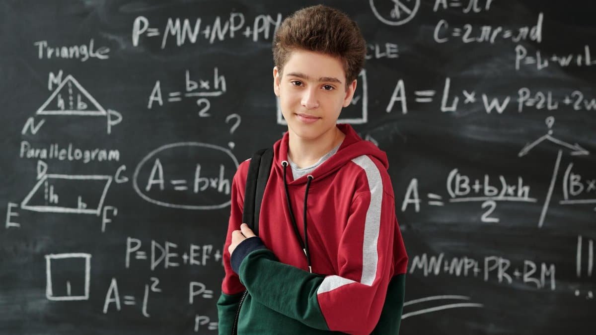 Teenage boy standing confidently in front of a blackboard filled with math formulas, showcasing his passion for learning.