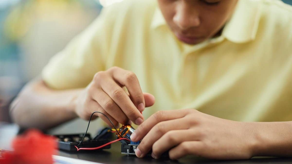 Close-up of a teenager building a robotics project, focusing on electronics and repairs.