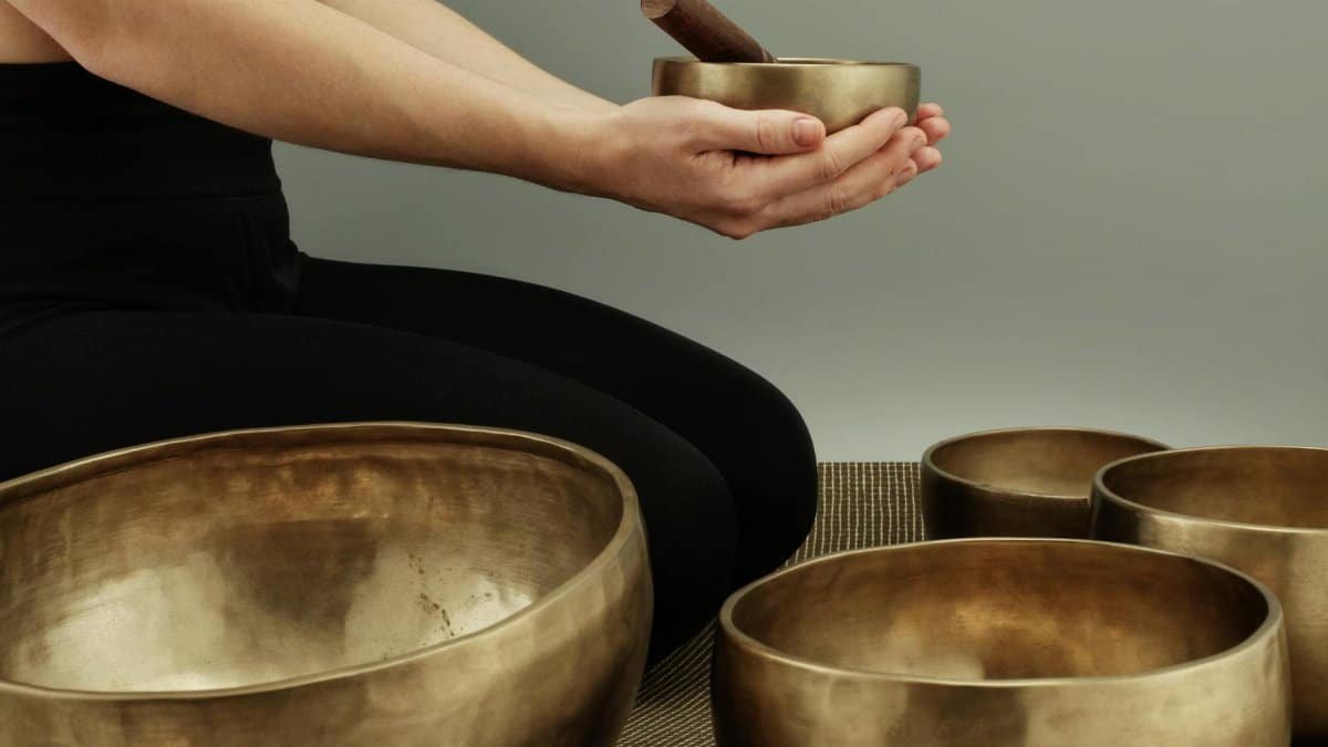 A person using bronze singing bowls for meditative sound therapy in a calm setting.