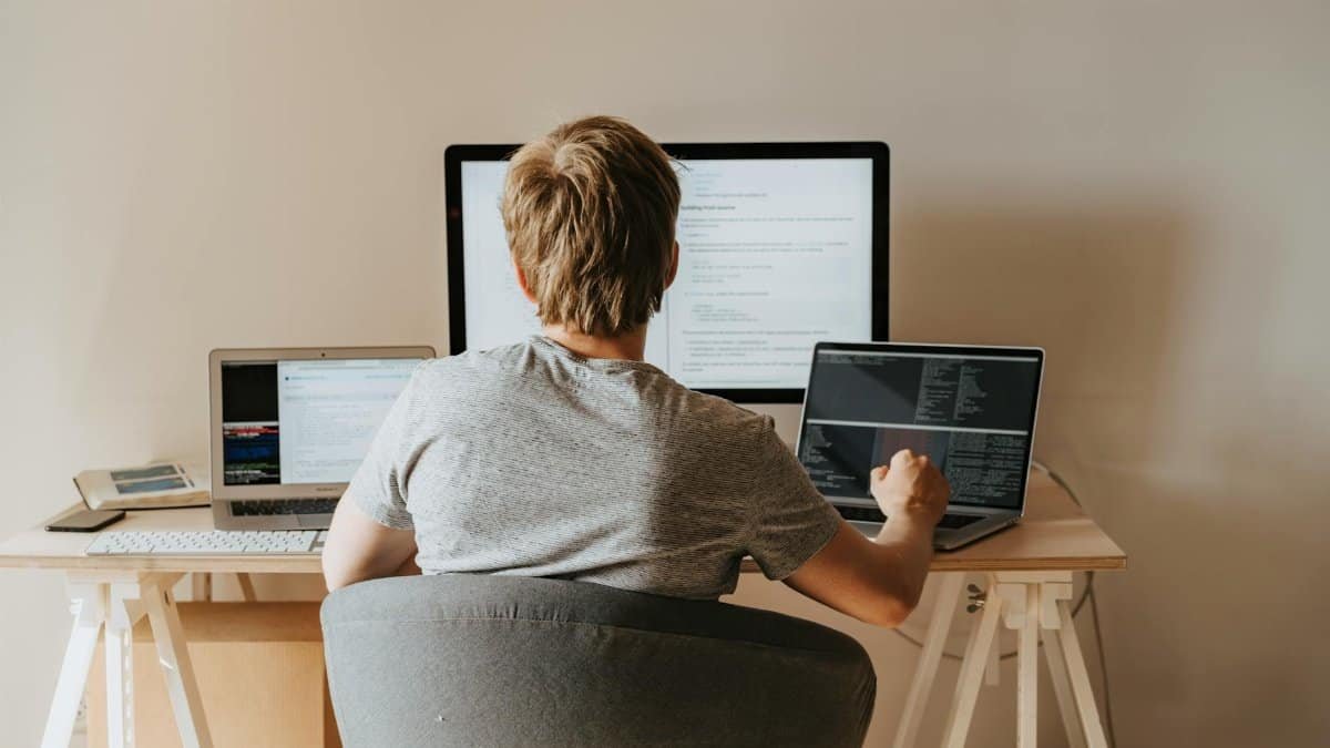 Teen programming with multiple laptops in a modern workspace. Ideal for tech and education themes.