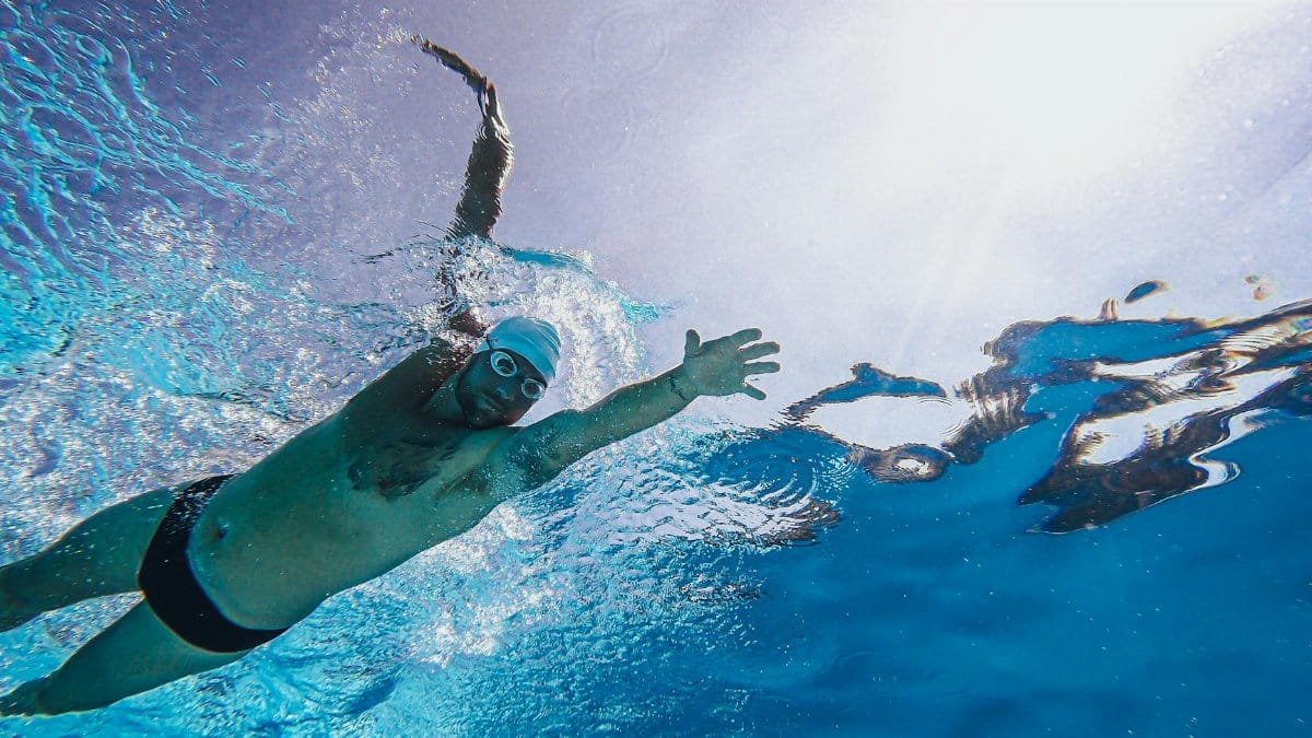 A male swimmer performing a freestyle stroke underwater with sunlight streaming above, showcasing intense athleticism.