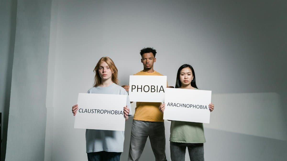 Three individuals holding signs representing various phobias, raising awareness.