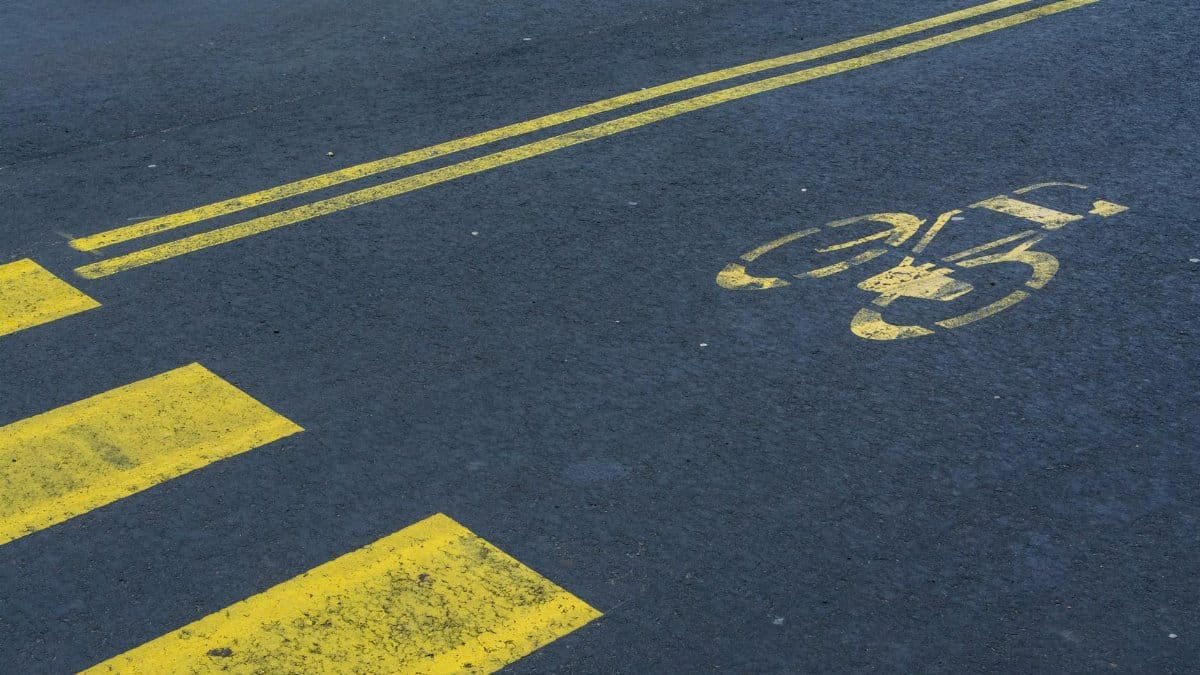 Bike lane with yellow markings on an empty asphalt road, showing bicycle symbol and zebra crossing.