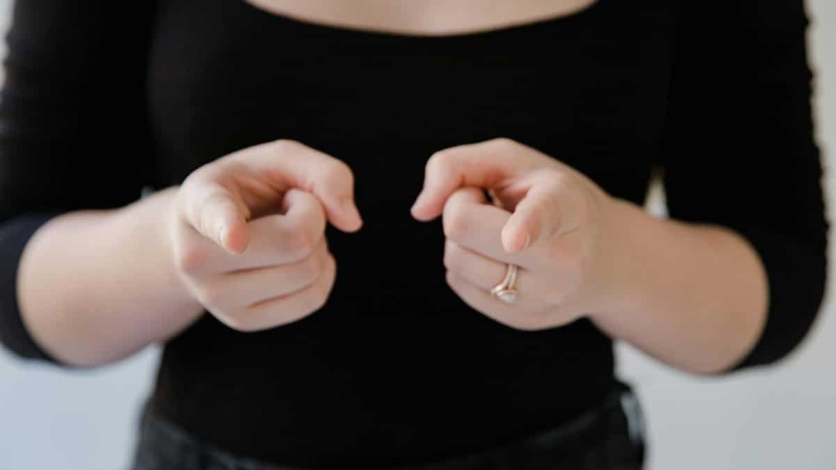A woman gestures with hands in a close-up shot, wearing a black outfit indoors.