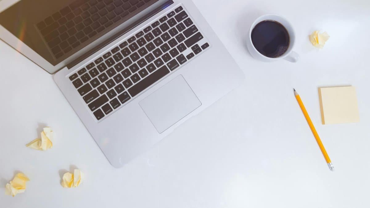 Top view of a minimalist workspace with a laptop, coffee cup, pencil, and crumpled paper.