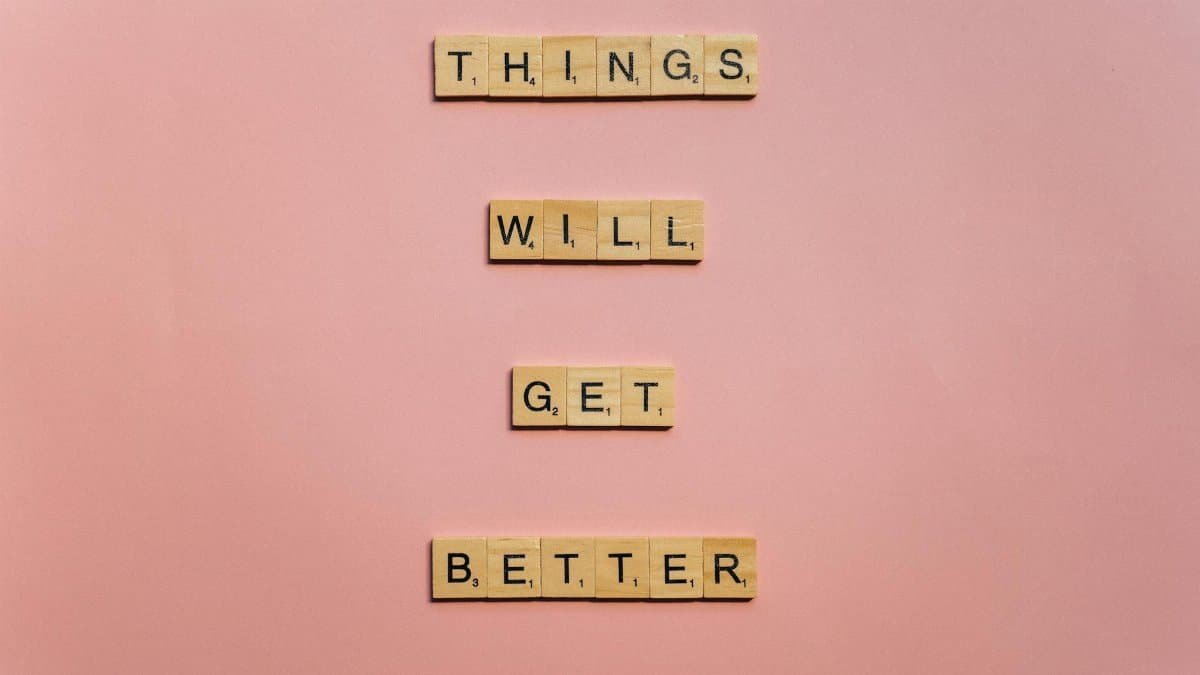 Inspirational words 'Things will get better' arranged in Scrabble tiles against a pink backdrop.