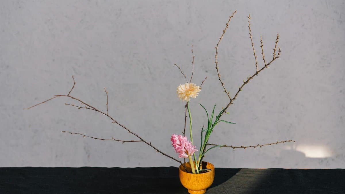 A serene minimalist floral arrangement in a wooden vase with branches and blooms.