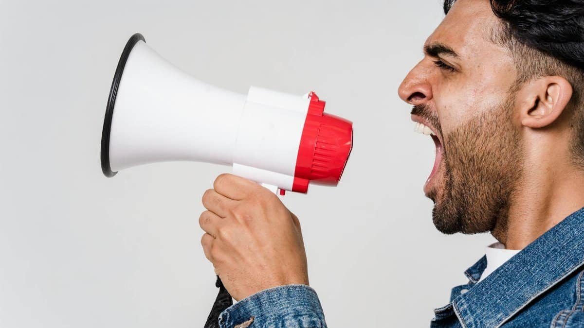 Close-up side view of a man shouting passionately into a megaphone, expressing urgency.