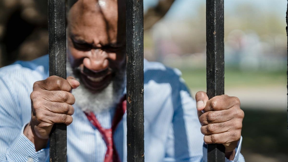 A frustrated man gripping metal bars outdoors, expressing anger and determination.