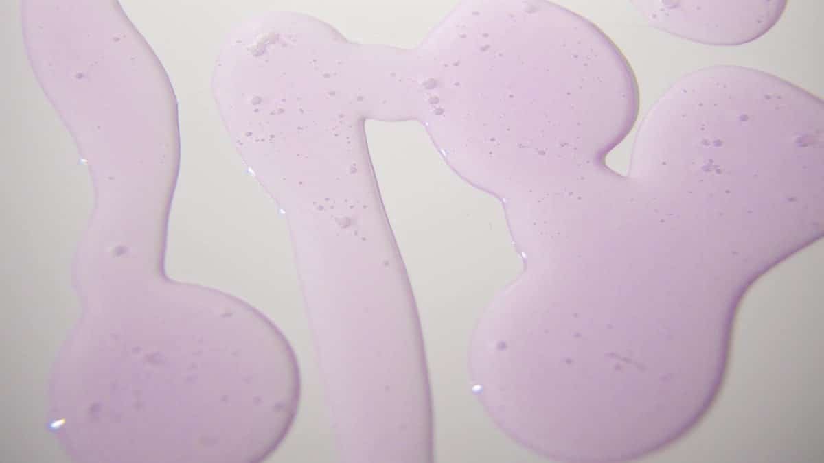 Abstract pattern of purple liquid on a smooth white background, offering vibrant texture and dynamic flow.