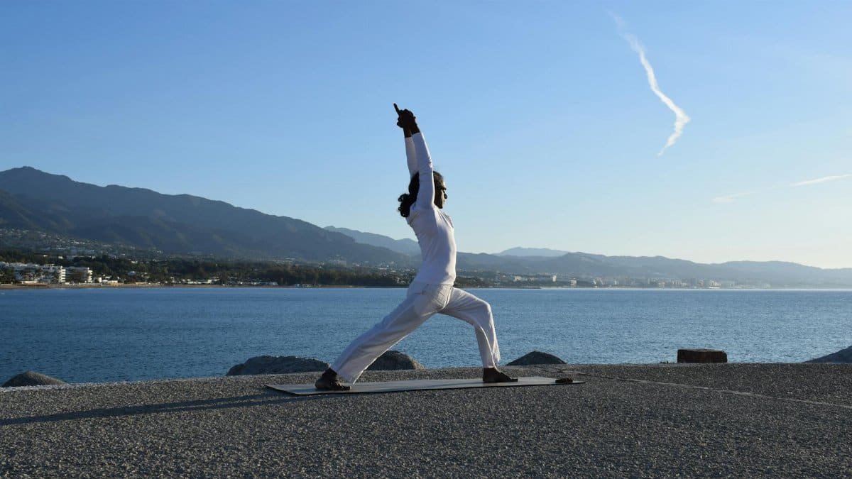 A man doing yoga on a mat by the ocean under a clear blue sky.