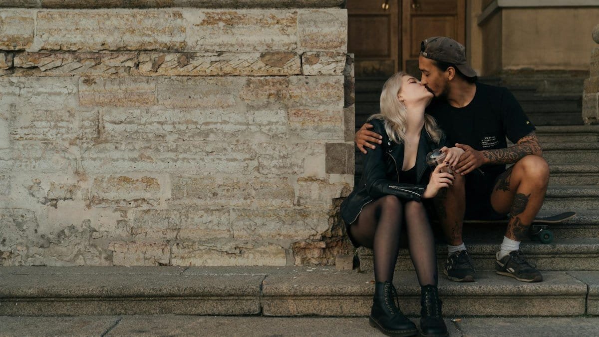 A couple sits on steps, sharing an intimate kiss, epitomizing modern romance.