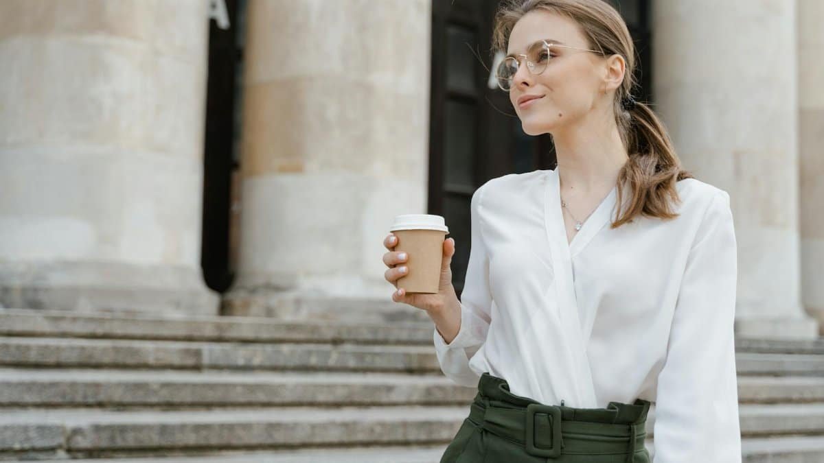 Elegant woman holding coffee cup, enjoying a casual day outdoors on stone steps.