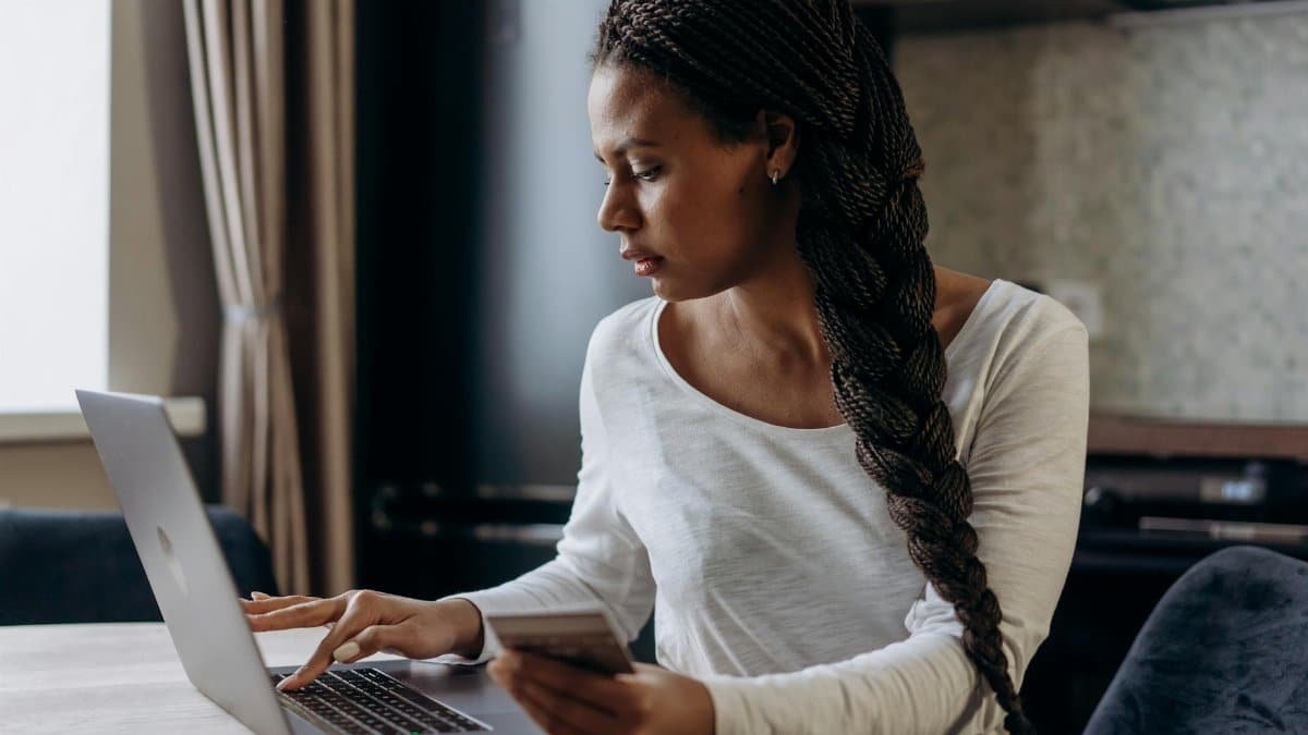Young African American woman with braided hair making an online payment using laptop and credit card.