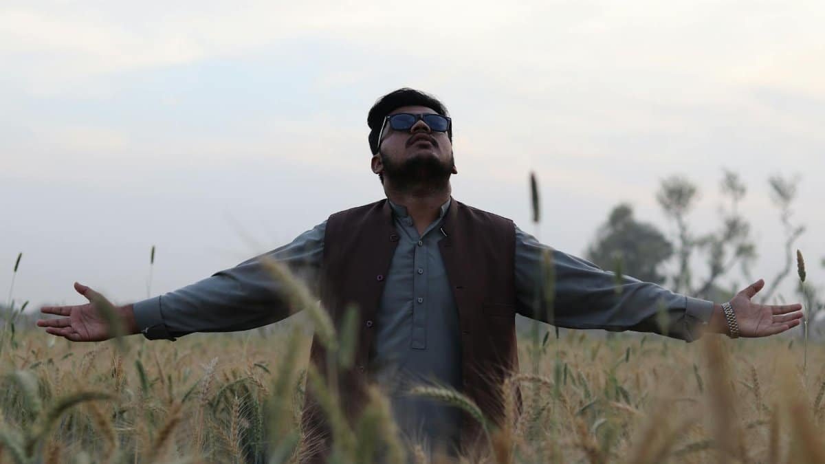 A man joyfully embraces nature in a rural wheat field under a vast sky, symbolizing peace and freedom.
