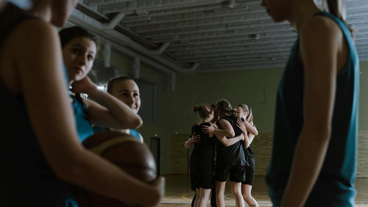 Women's basketball team sharing a victorious embrace on an indoor court after a game.