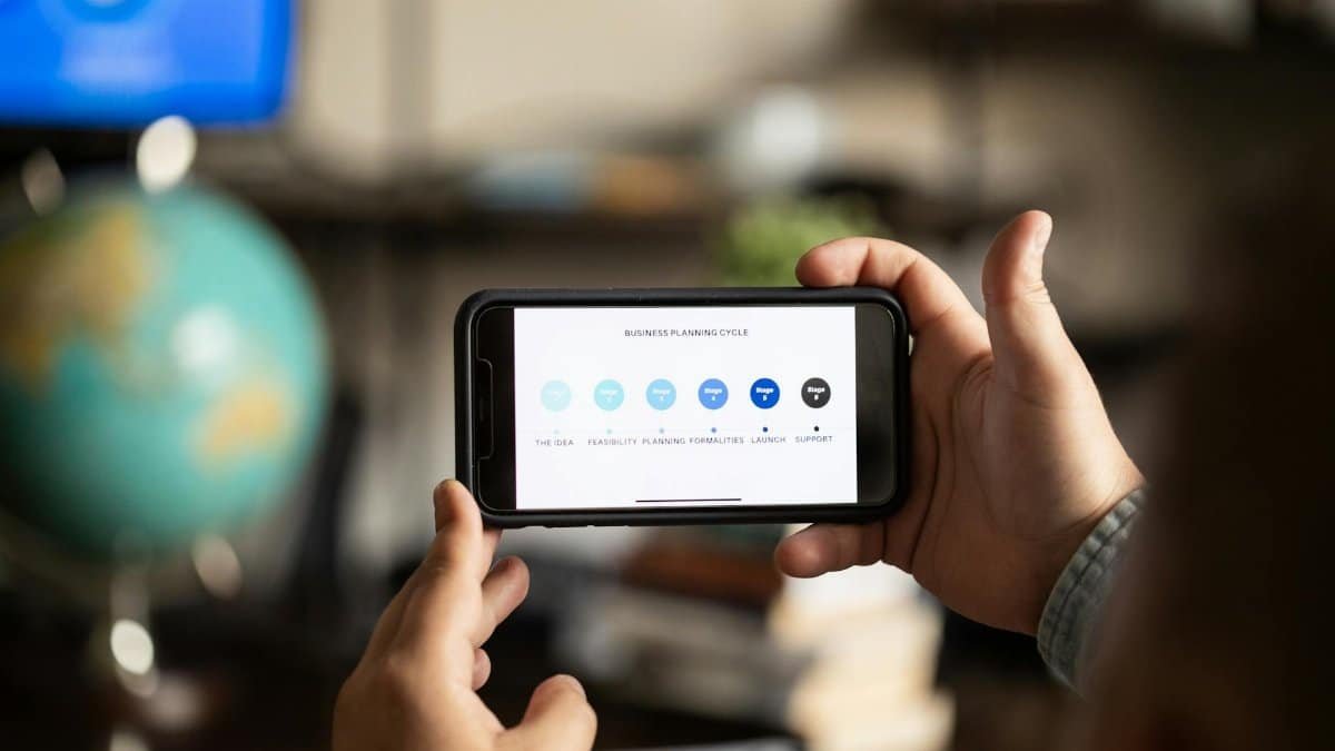 Close-up of hands holding a smartphone displaying a business planning cycle diagram.