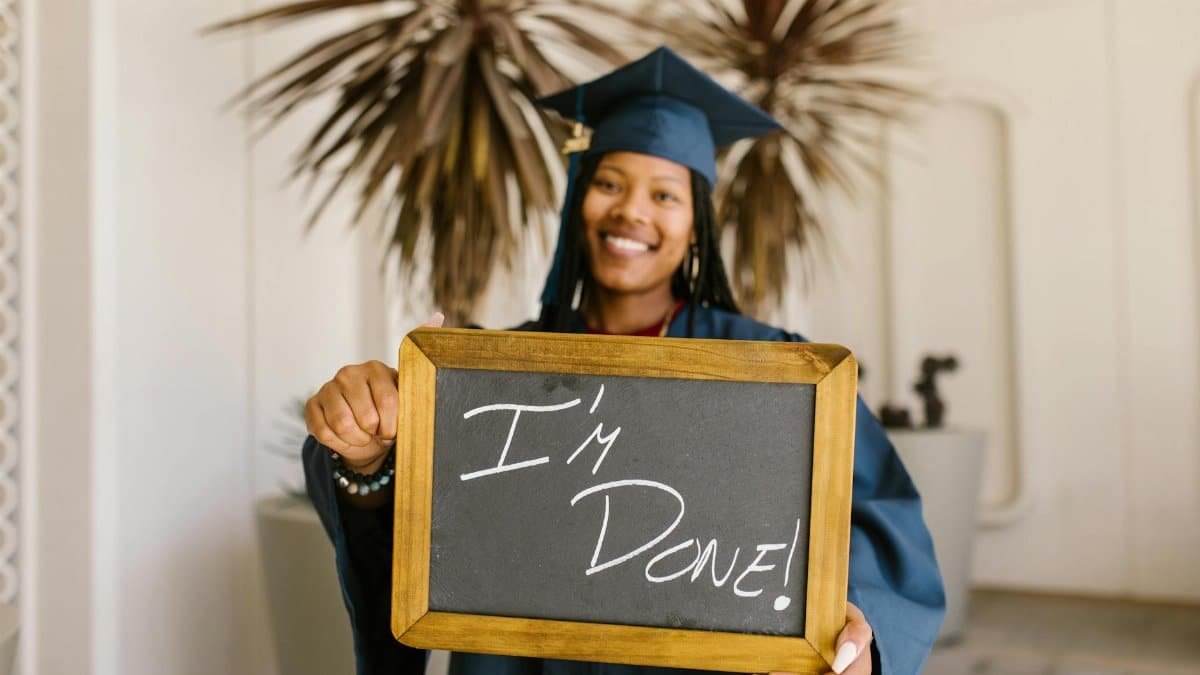 A proud graduate holds a mini blackboard with 'I'm Done!' indoors, celebrating academic success.