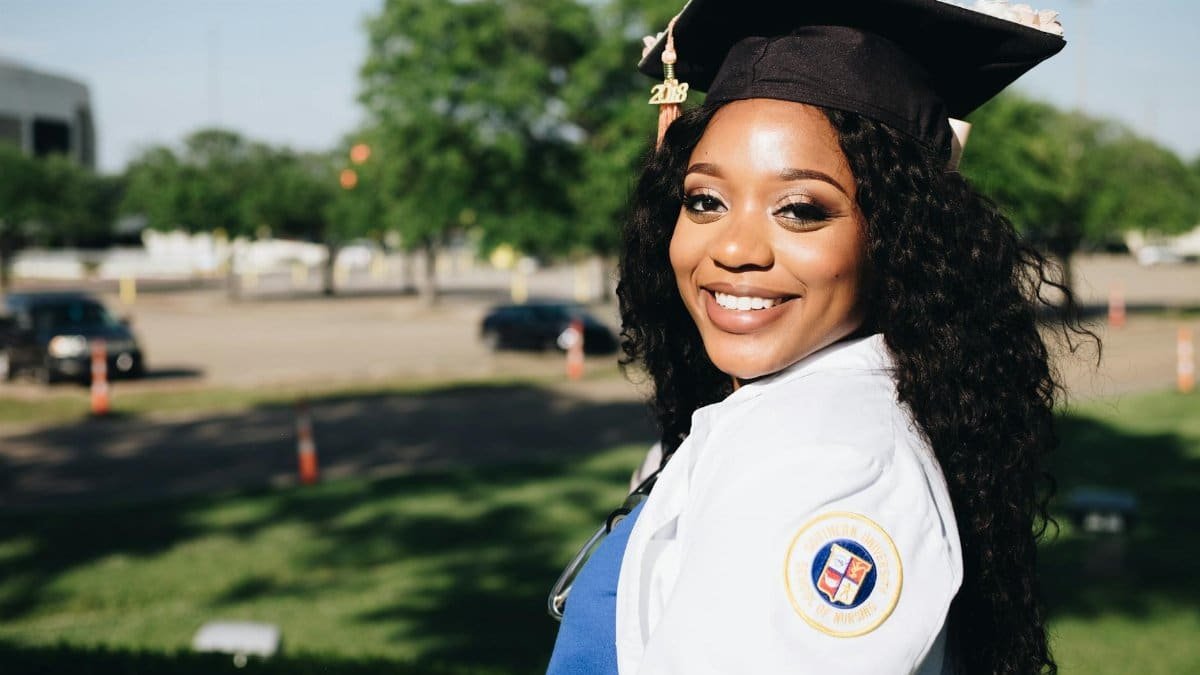 African American woman in graduation attire, smiling outdoors, symbolizing academic success.