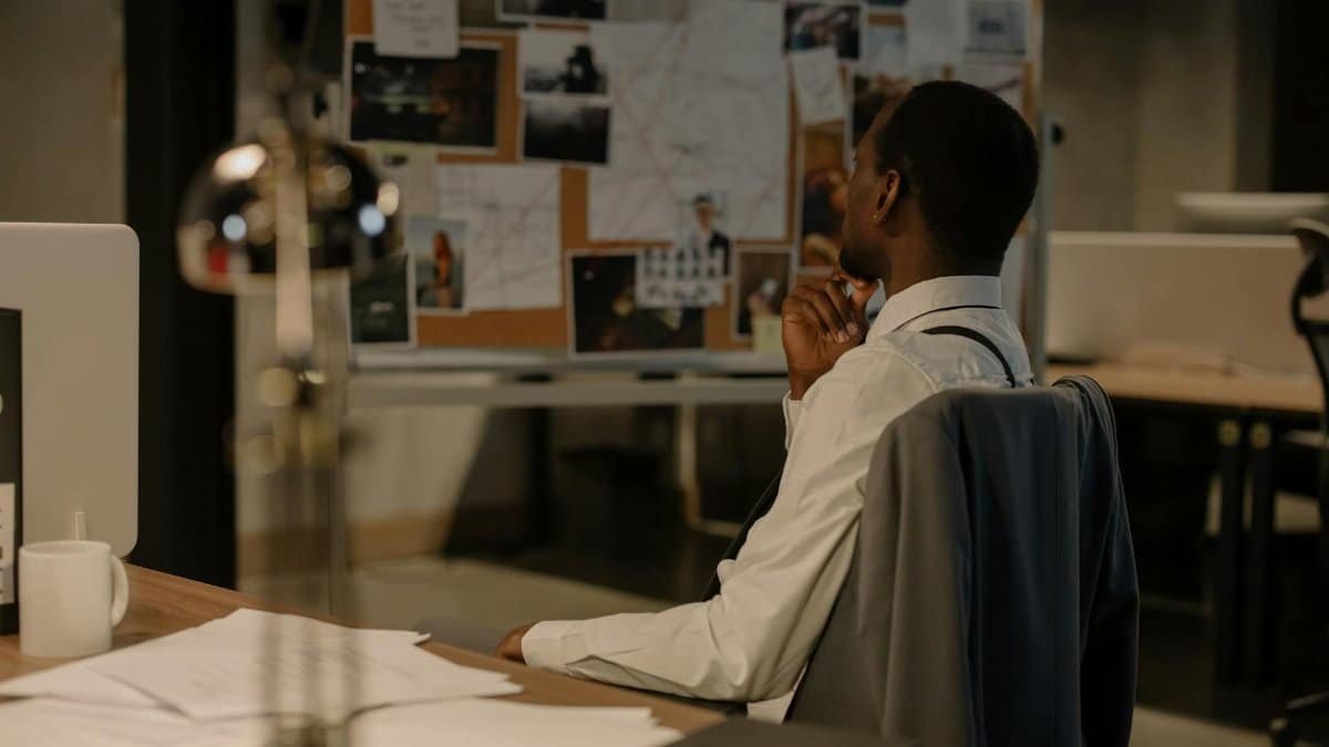 Detective in thought examining evidence board in a dimly lit office environment.