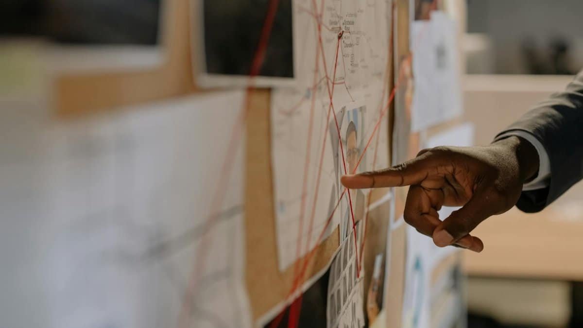 Close-up of an investigator pointing at an evidence board with connected clues using red strings.