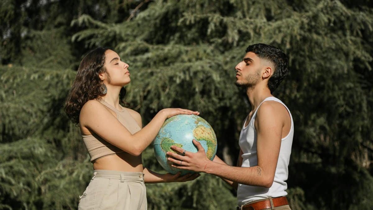 A young couple holds a globe outdoors, symbolizing unity and cooperation.
