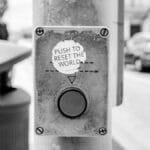 Grayscale photo of a street button labeled 'Push to reset the world', Lisbon urban scene.