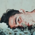 An ethereal portrait of a young adult male lying among flowers, conveying themes of vulnerability and mental health.