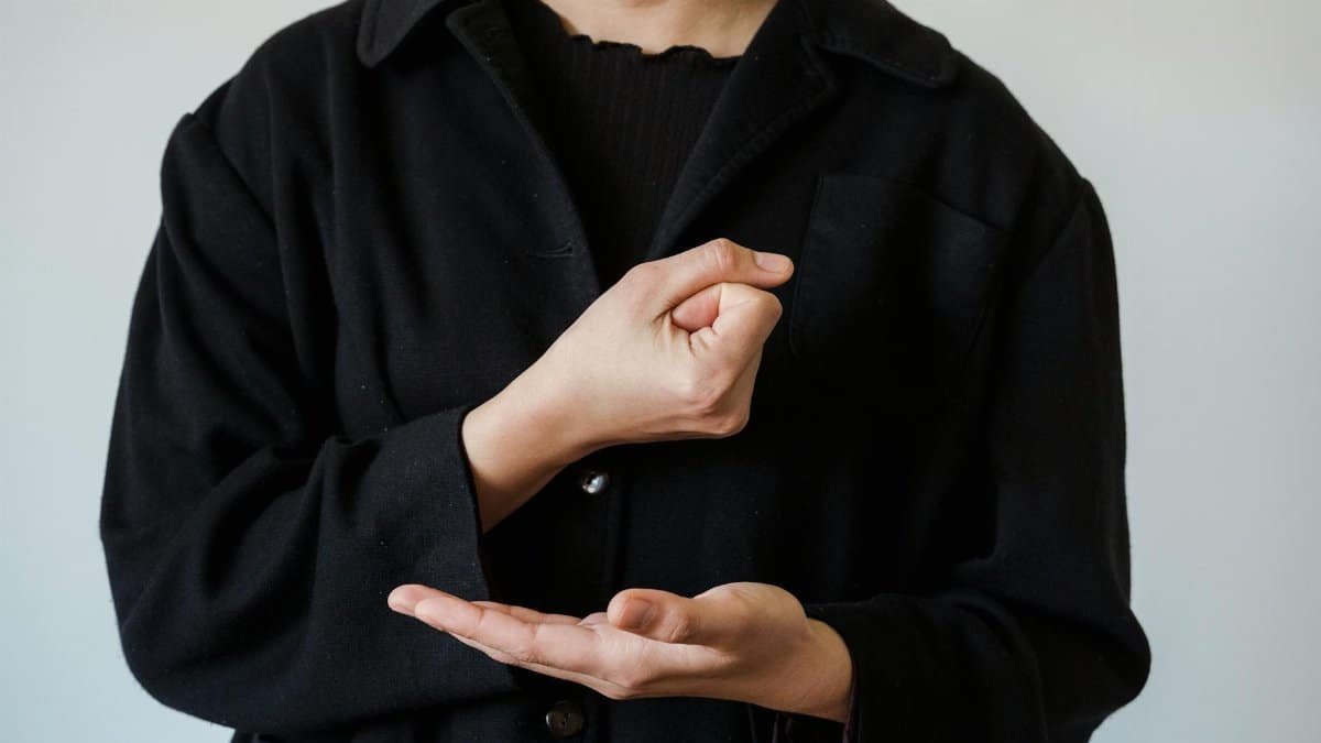 Person demonstrating American Sign Language in a black jacket, focusing on hand gestures.