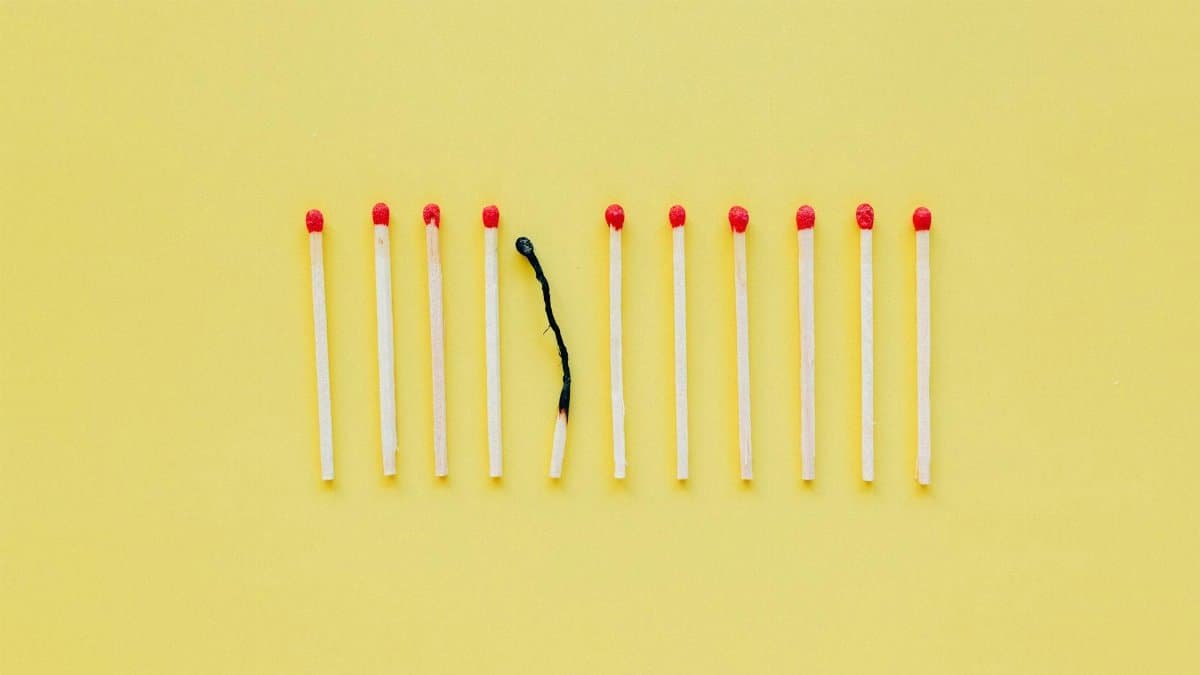 A burnt matchstick among unlit ones symbolizes burnout on a yellow background.