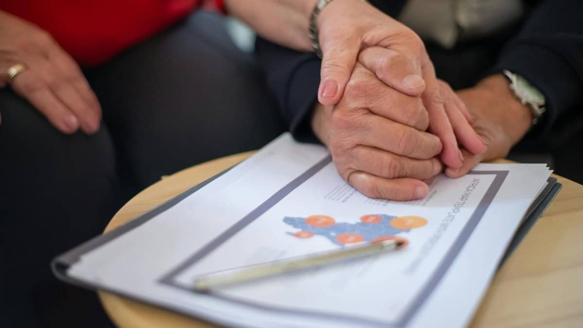 Two adults holding hands over business documents, symbolizing support and partnership.