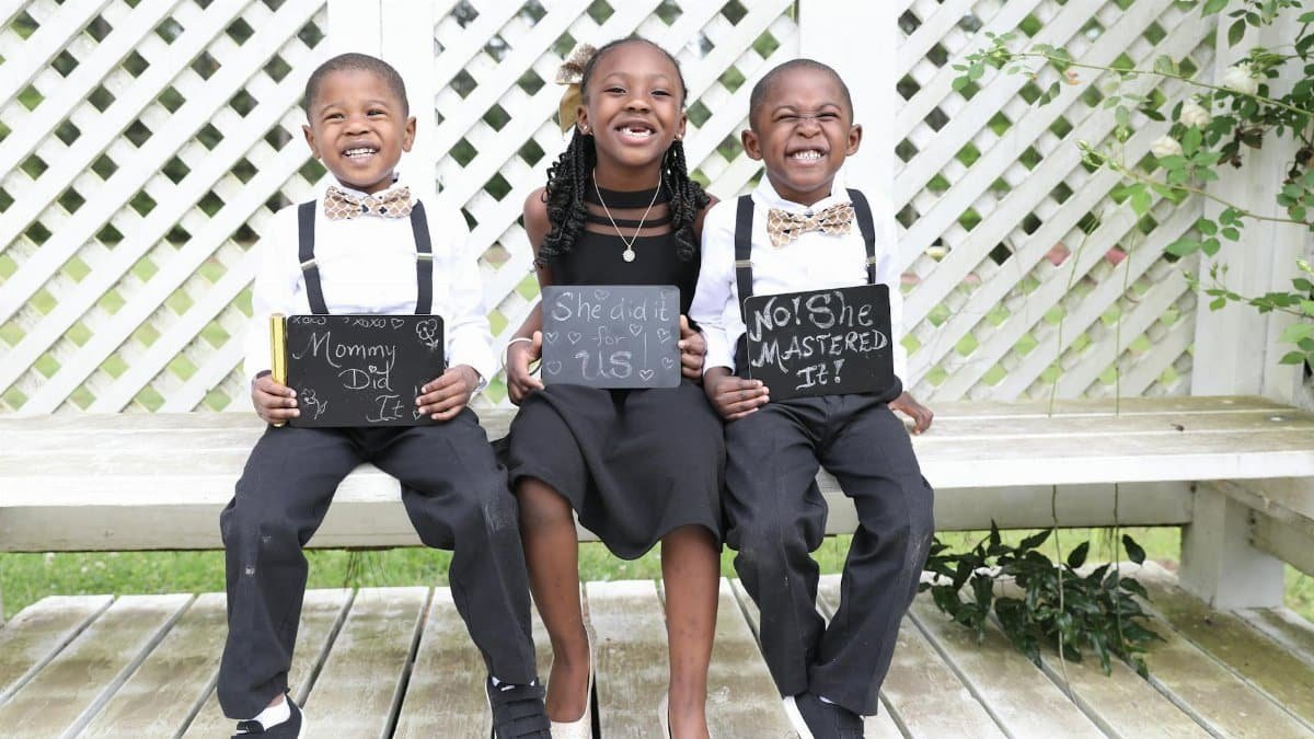 Three children smiling with signs, celebrating achievements in a garden setting.