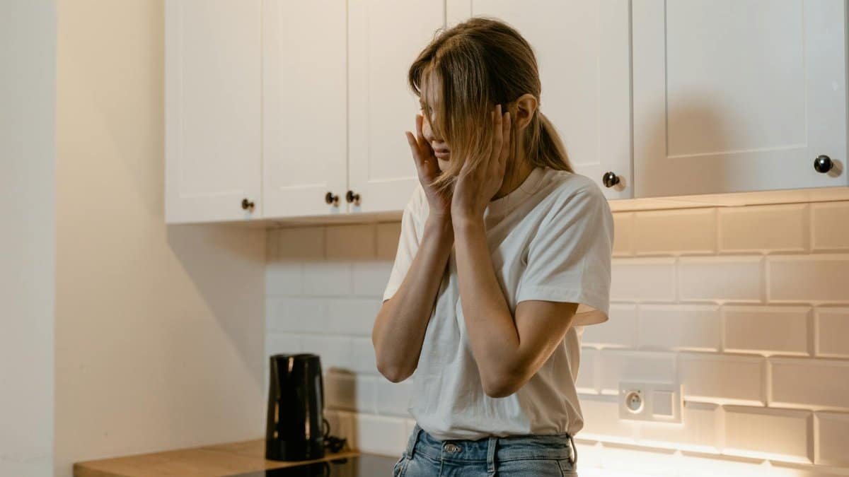 A woman in a modern kitchen looking distressed, emphasizing mental health awareness.