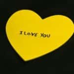 A yellow heart-shaped note with 'I Love You' text on a dark fabric background.