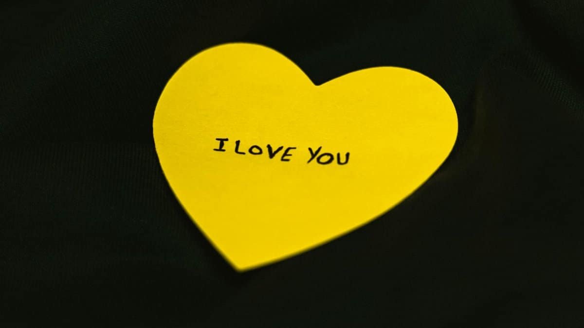 A yellow heart-shaped note with 'I Love You' text on a dark fabric background.
