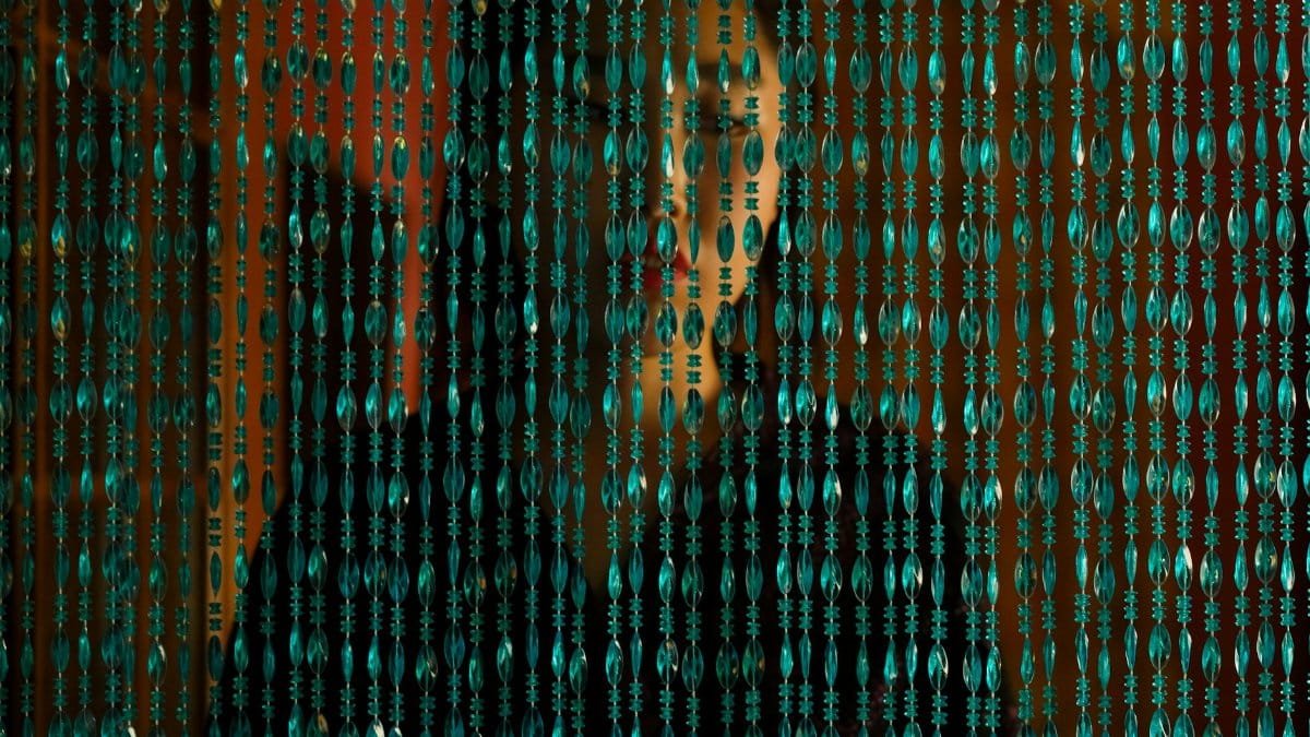 A woman stands behind a beaded curtain, creating a mysterious and elegant atmosphere.
