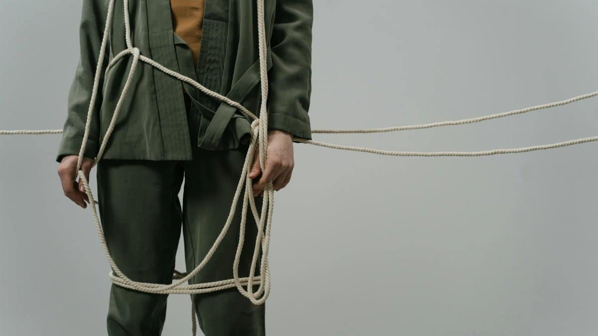 A captivating conceptual photograph showing a person in green clothes tangled with ropes, symbolizing entrapment or struggle.