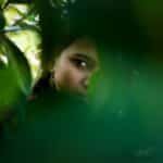 A woman partially hidden within lush green leaves, creating a sense of mystery.